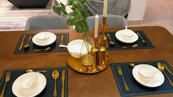 Een eettafel gedekt met goudkleurig en wit servies, een vaas met groene takken en kaarsen.
