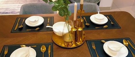 A dining table set with gold and white tableware, a vase with green foliage, and candles.