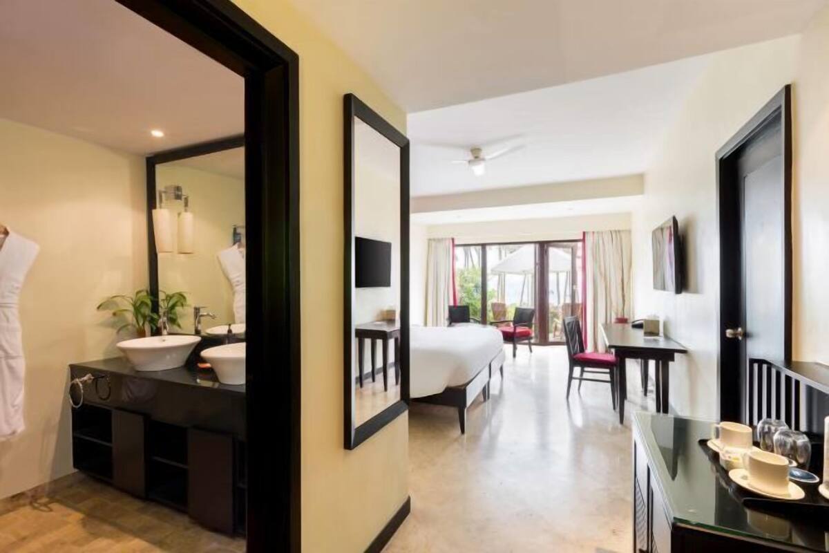 Ein Hotelzimmer mit einem großen Bett, einem Schreibtisch mit Stuhl, einem Badezimmer mit Waschbecken und Spiegel sowie Blick ins Freie.