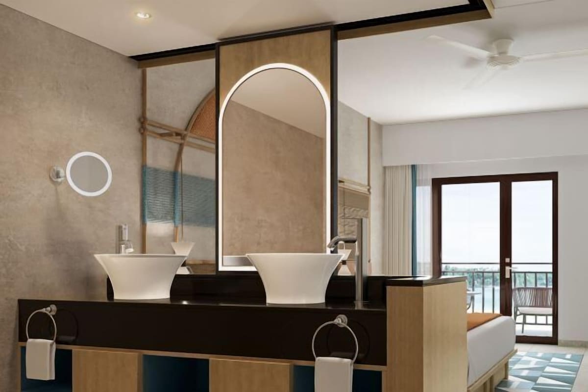 Un baño moderno con un espejo grande, dos lavamanos y un ventilador de techo.