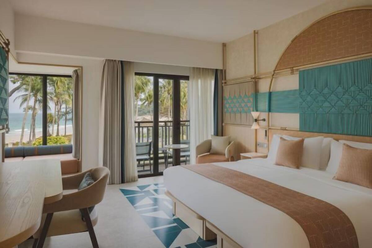Ein Hotelzimmer mit einem großen Bett, einem Schreibtisch und einem Balkon mit Blick auf den Strand.