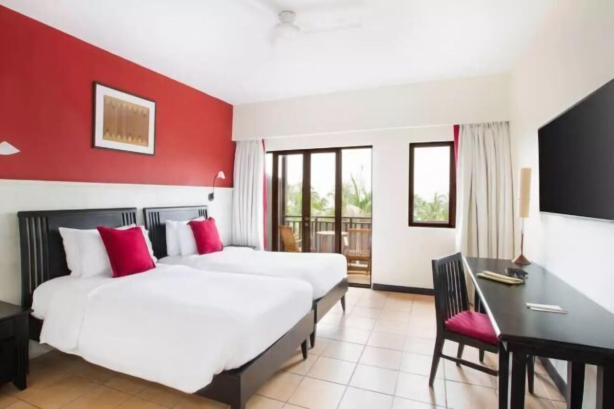 A hotel room with two beds, a desk, and a balcony with a view.