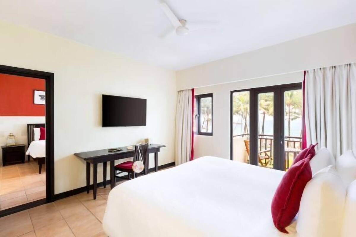 Ein Hotelzimmer mit Bett, Schreibtisch, Stuhl, Fernseher und einem Balkon mit Vorhängen.
