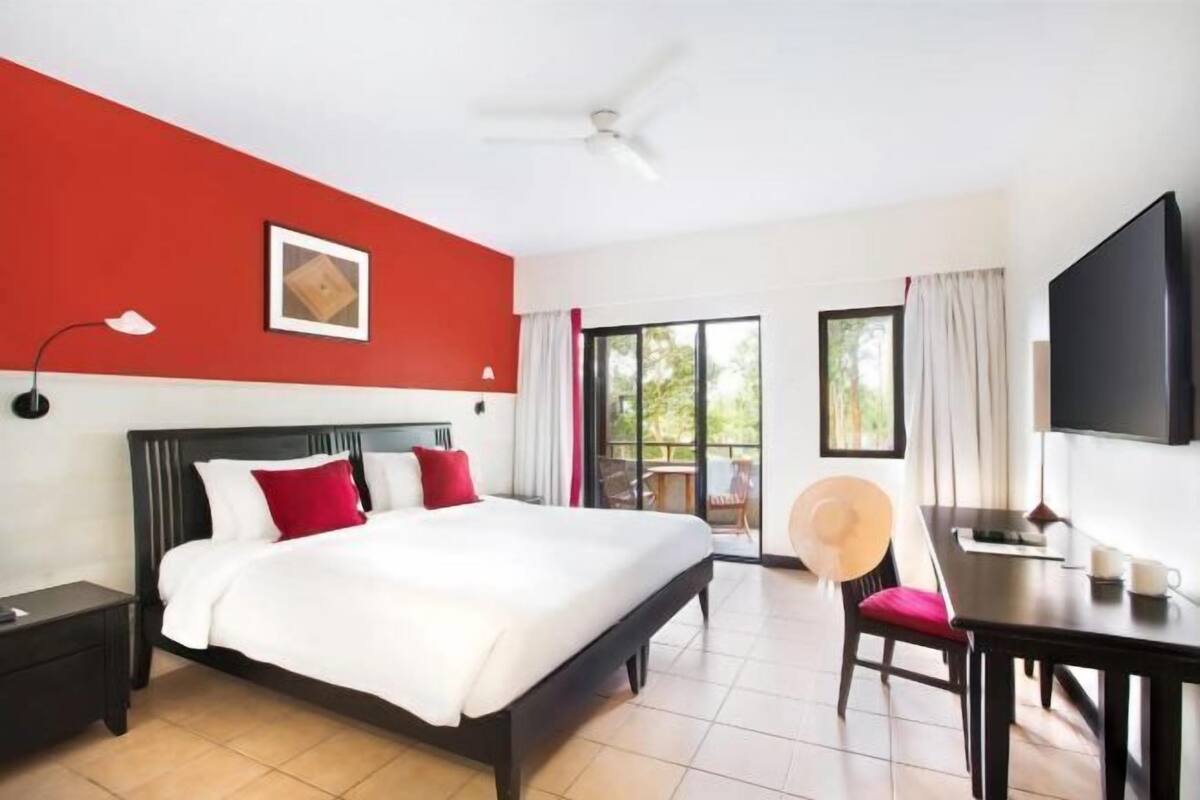 Ein Hotelzimmer mit Bett, Schreibtisch, Stuhl, Fernseher und Deckenventilator.