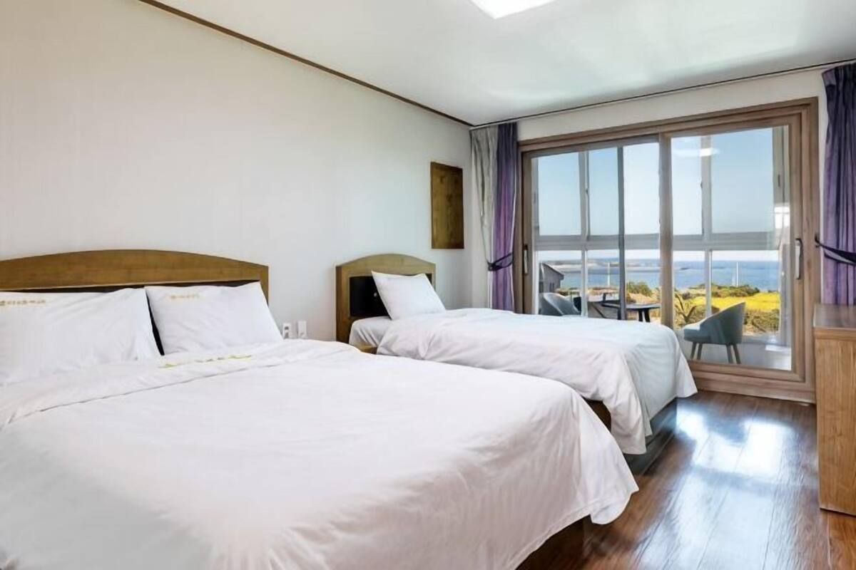 Une chambre d’hôtel avec deux lits, une grande fenêtre donnant sur un beau paysage et un balcon avec des sièges pour profiter de l’extérieur.