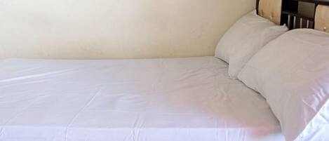 Un lit simple avec une tête de lit en bois et du linge de lit blanc.