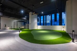 Een ruimte binnenshuis met een gedeelte kunstgras, grote ramen en een plafondventilator.