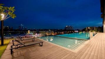 A rooftop pool with a wooden deck and lounge chairs.