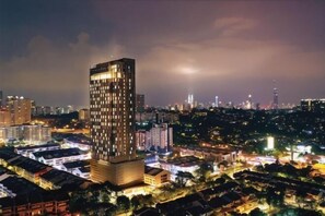 Un immeuble de grande hauteur, doté d’une façade à motifs géométriques de fenêtres, se dressant au milieu d’un paysage urbain nocturne.