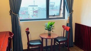 Ein Zimmer mit Fenster, zwei Stühle, einem kleinen Tisch mit Pflanze und einem Heizkörper.