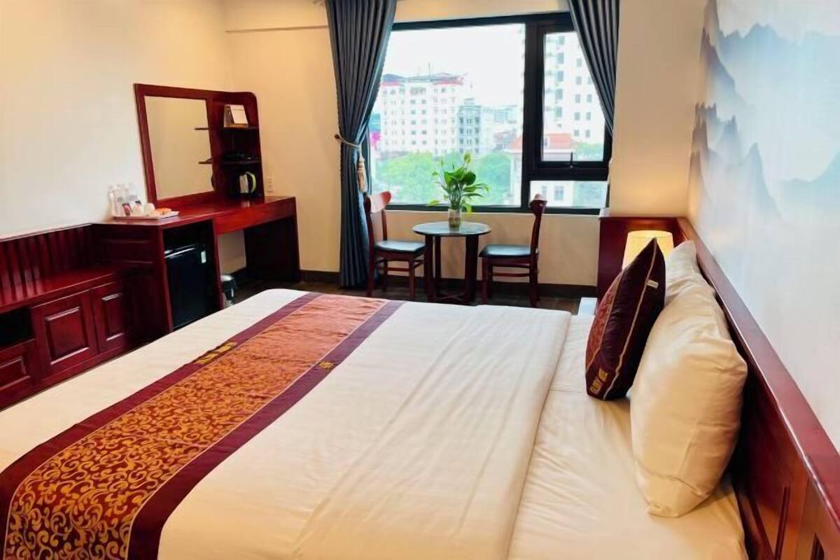 Une chambre d’hôtel comprenant un lit, un bureau, une chaise, une petite table et une fenêtre donnant sur des immeubles.