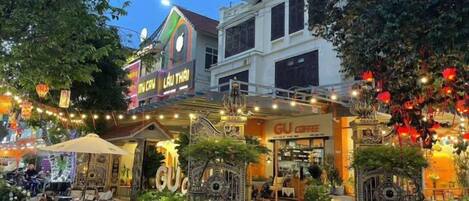 A building with a restaurant and outdoor seating area, surrounded by trees and decorated with lights.