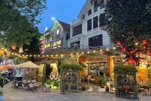 A building with a restaurant and outdoor seating area, surrounded by trees and decorated with lights.