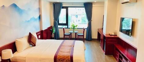 A hotel room with a bed, a desk, a chair, a TV, and a window with curtains.