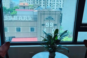 Uitzicht vanuit een raam, met een plant op een tafel, met zicht op een gebouw met de aanduiding '99' en 'Palace'.