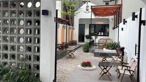 Ein Sitzbereich im Freien mit Tischen und Stühlen, ein kleiner Garten und ein Gebäudeeingang mit der Aufschrift "LAM TRON COFFEE".