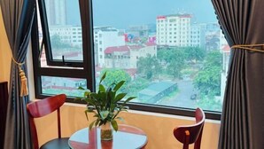 Ein Zimmer mit großem Fenster, einem runden Tisch, zwei Stühlen und einem Blumentopf.