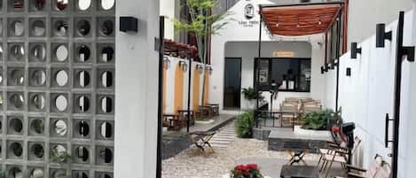 Entrada a una cafetería con un letrero que dice 'LAM TRON COFFEE', mesas y sillas para disfrutar al aire libre, y un pequeño jardín con flores.