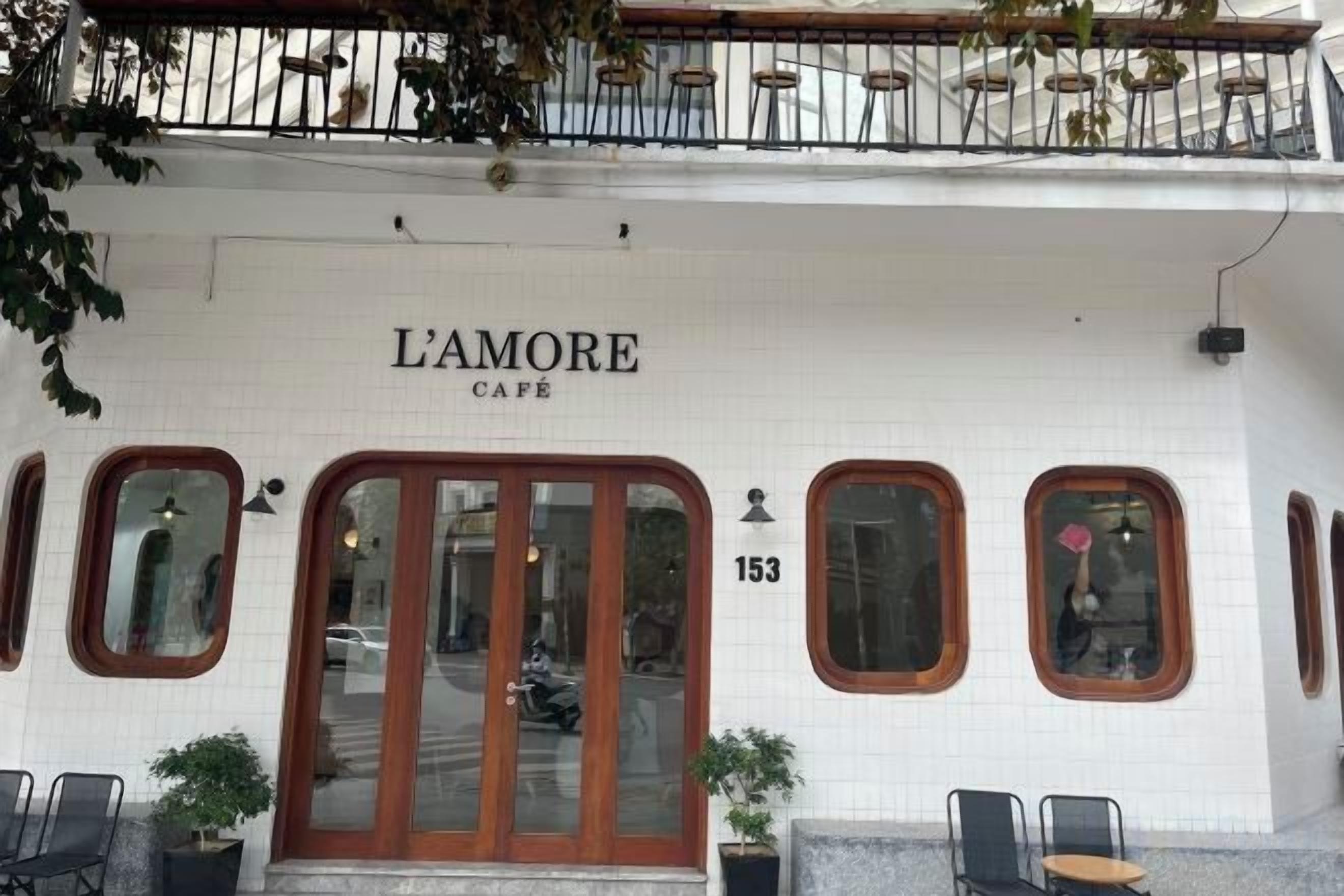 Ein Café namens 'L'Amore' mit weißer Fassade, Hausnummer 153, und einem Balkon mit Sitzgelegenheiten im Freien.