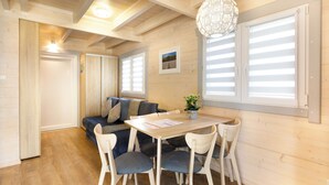 A cozy room with a wooden floor, a dining table with chairs, a sofa with cushions, and a hanging light fixture. - Collins Resorts are dream vacations for families with children right on the beach. (Sianożęty)