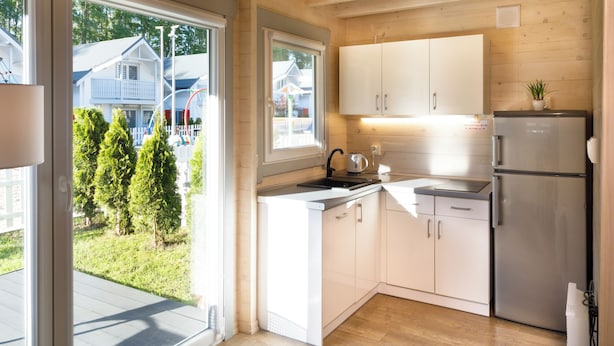 A modern kitchen with white cabinets, a stainless steel refrigerator, and a view of a residential area through large windows. - Collins Resorts are dream vacations for families with children right on the beach. (Sianożęty)