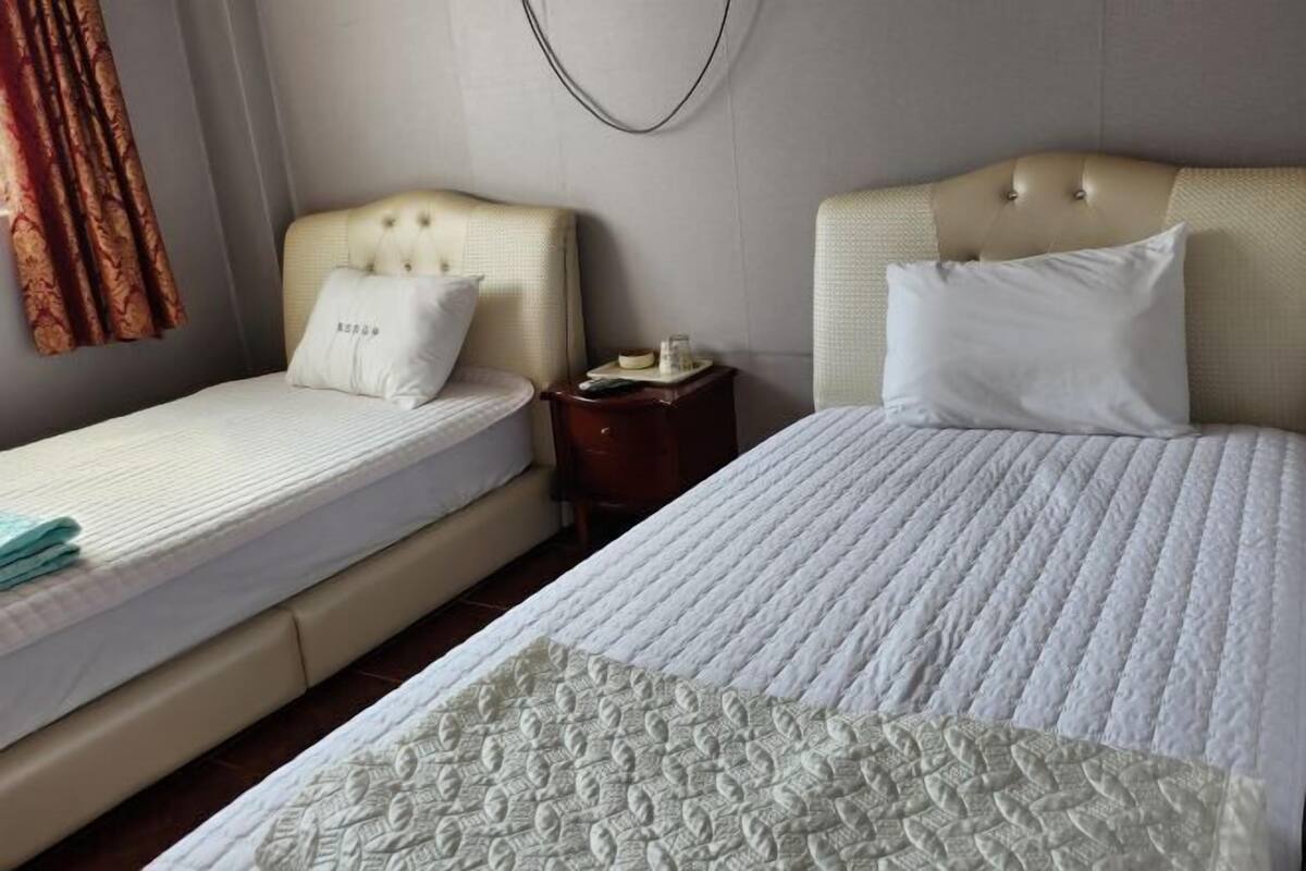 A hotel room with two beds, a small bedside table, and a wall-mounted light fixture.