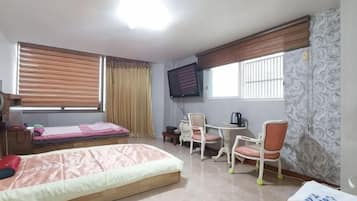 A room with a bed, a desk with chairs, a television, and a window with blinds.