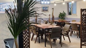A modern dining area with multiple tables and chairs, a large potted plant, and a giraffe statue. - BUSAN YONGDO HAYANSUNG HOTEL (Busan)