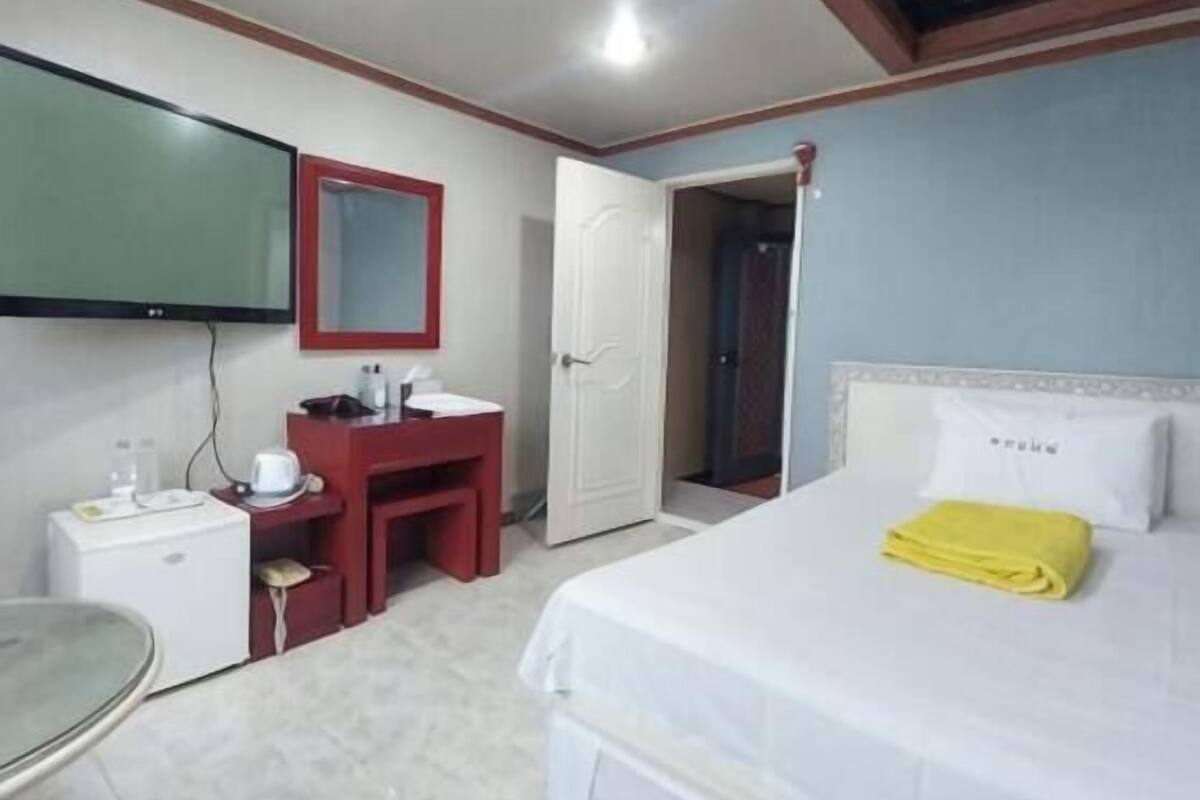 A hotel room with a bed, a desk with a mirror, a small table, and a television mounted on the wall.
