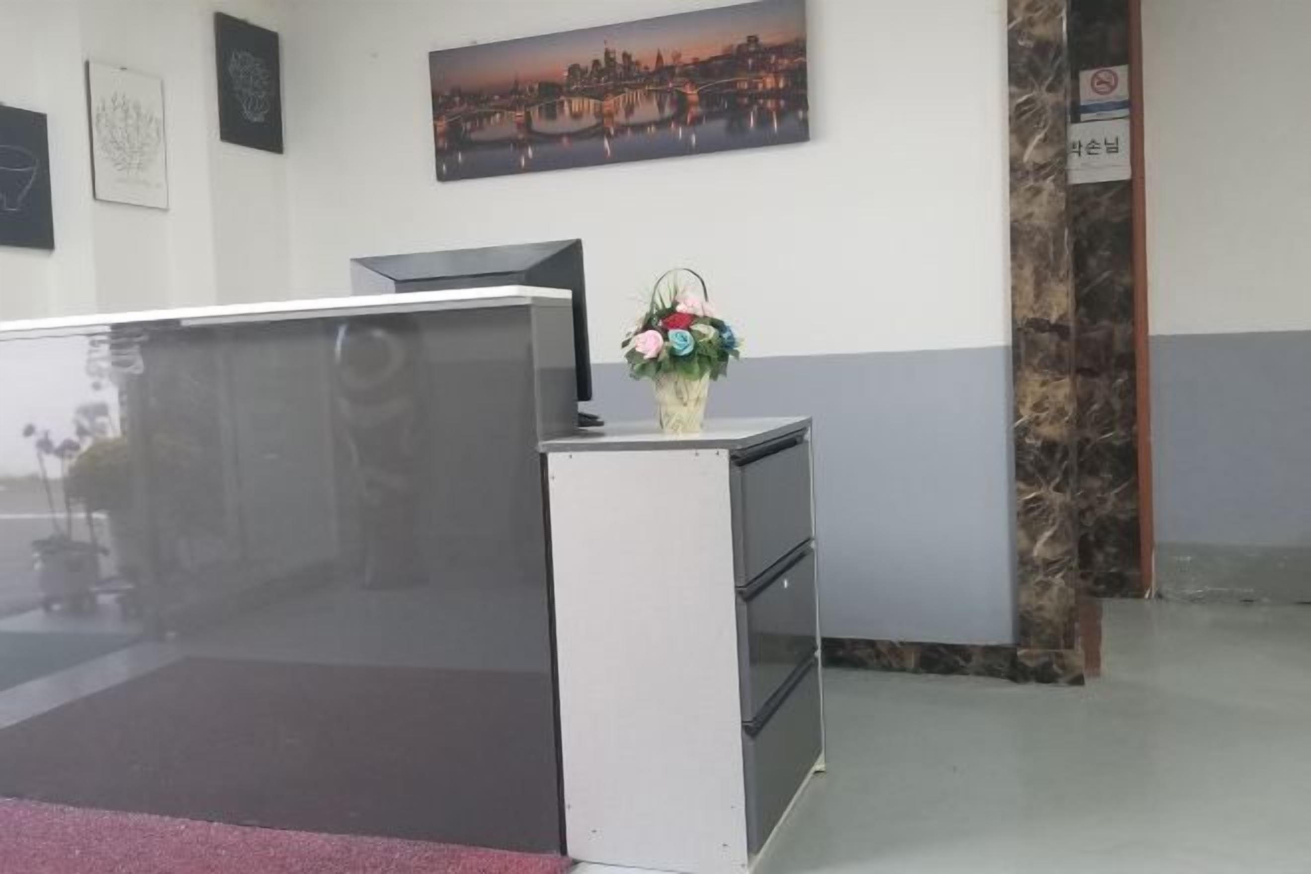 A reception desk with a vase of flowers, a cityscape painting, and a no-smoking sign.