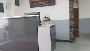 A reception desk with a vase of flowers, a cityscape painting, and a no-smoking sign.