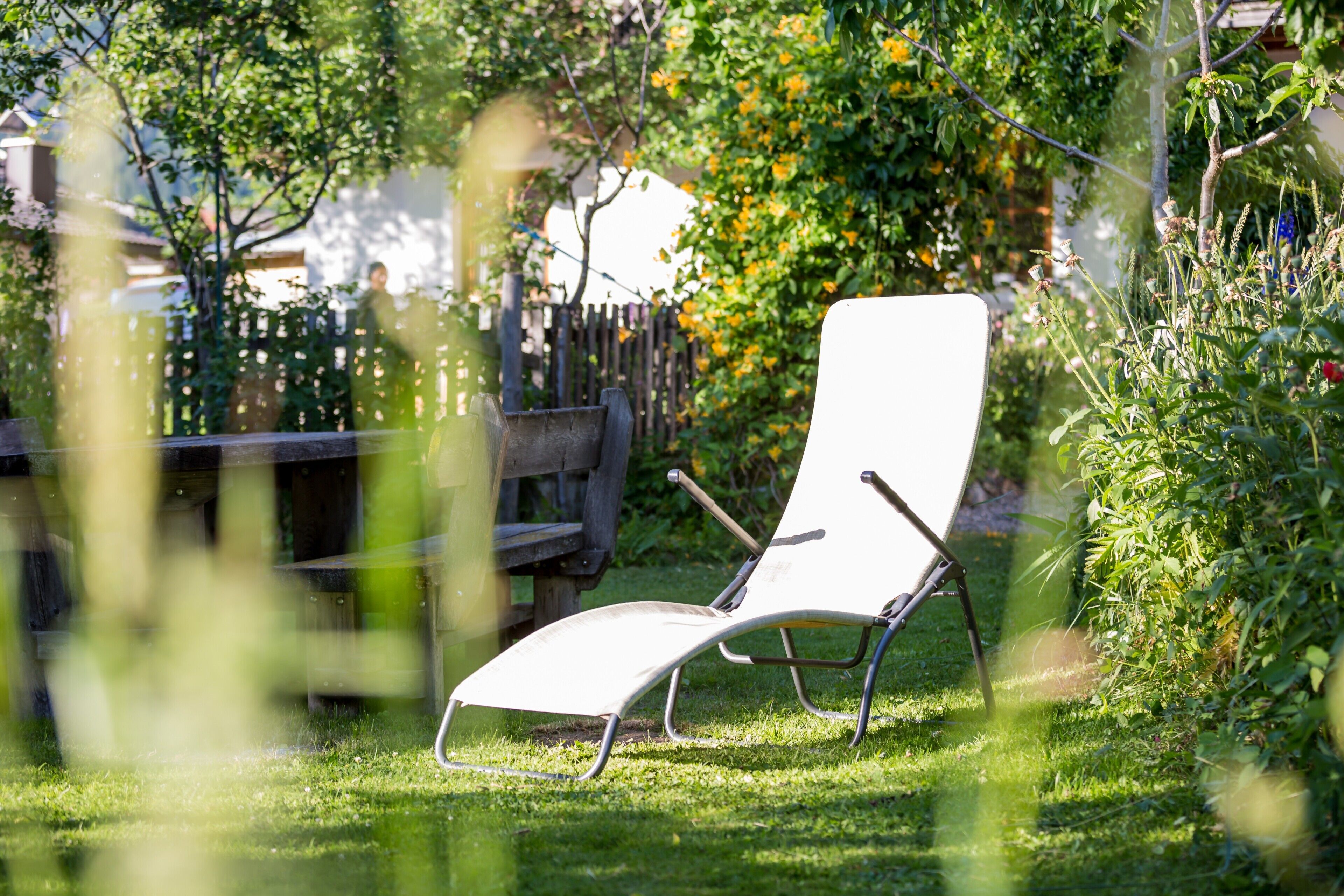 Uma cadeira de lounge branca em um jardim, com um banco de madeira e uma cerca ao fundo.