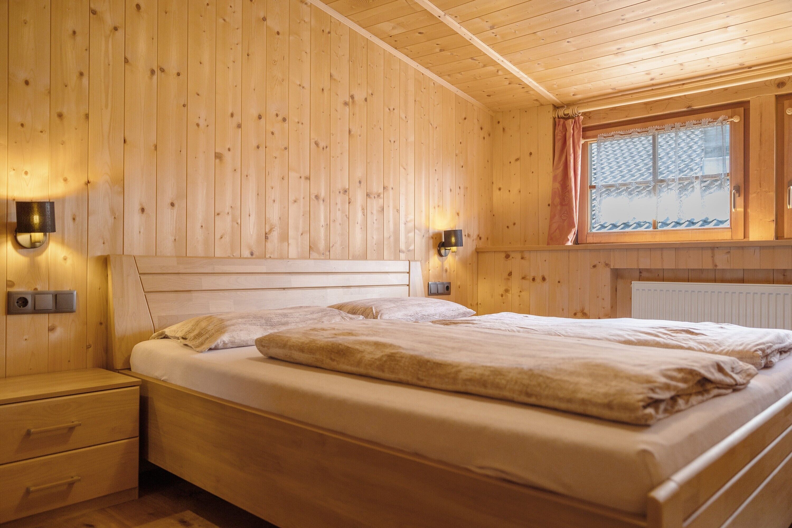 A wooden-paneled room with a bed, bedside tables, and a window with a view.