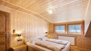 A wooden-paneled bedroom with a bed, nightstands, wall-mounted lights, and a window with curtains. - Apartment 'Jelerhof Hochstein' with Mountain View, Shared Garden and Wi-Fi (Gsies)