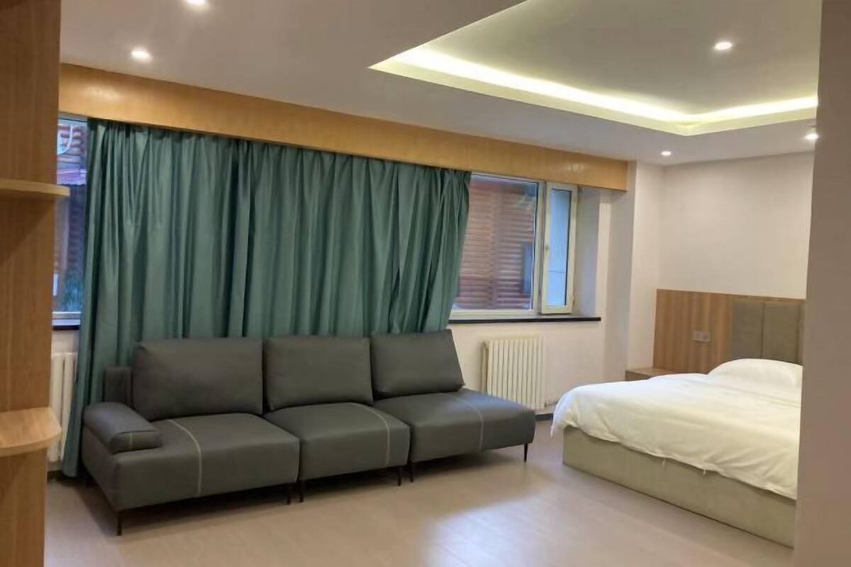 A modern bedroom with a grey sofa, a bed, and a window with curtains.