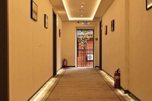 A hotel corridor with a carpeted floor, framed pictures on the walls, and a fire extinguisher on the right. - Yingbin Garden Hotel (Almaty)