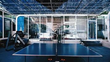 A ping pong table with exercise equipment and a glass wall.