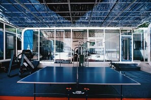 A ping pong table with exercise equipment and a glass wall. - Yingbin Garden Hotel (Almaty)