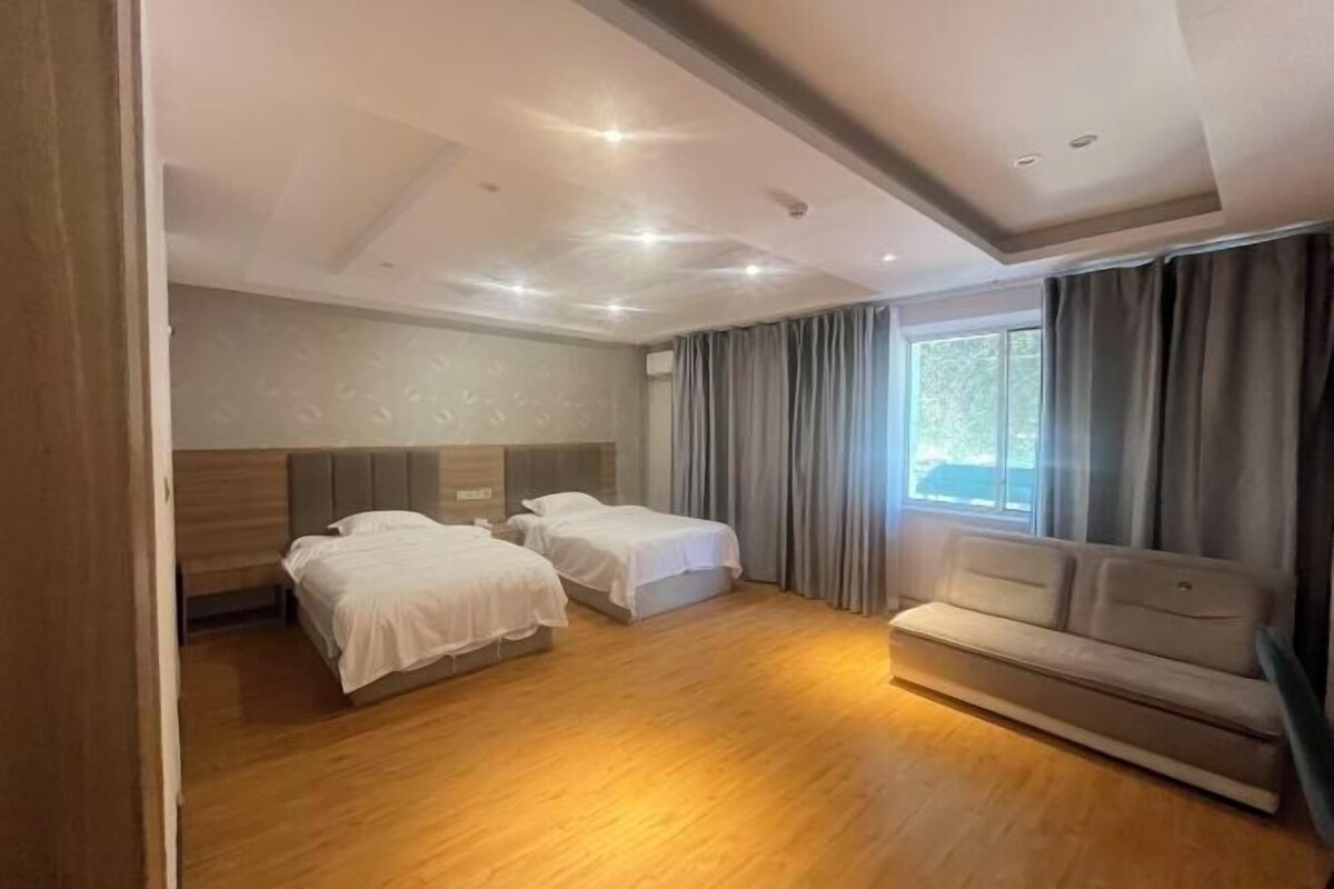 A hotel room with two beds, a sofa, and a large window with curtains.