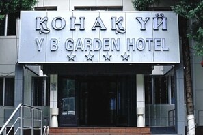The exterior of the Kohak Yi YB Garden Hotel with a prominent sign, a staircase leading to the entrance, and a modern building facade. - Yingbin Garden Hotel (Almaty)