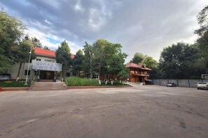 A building with a red roof, a signboard, and a paved entrance. - Yingbin Garden Hotel (Almaty)