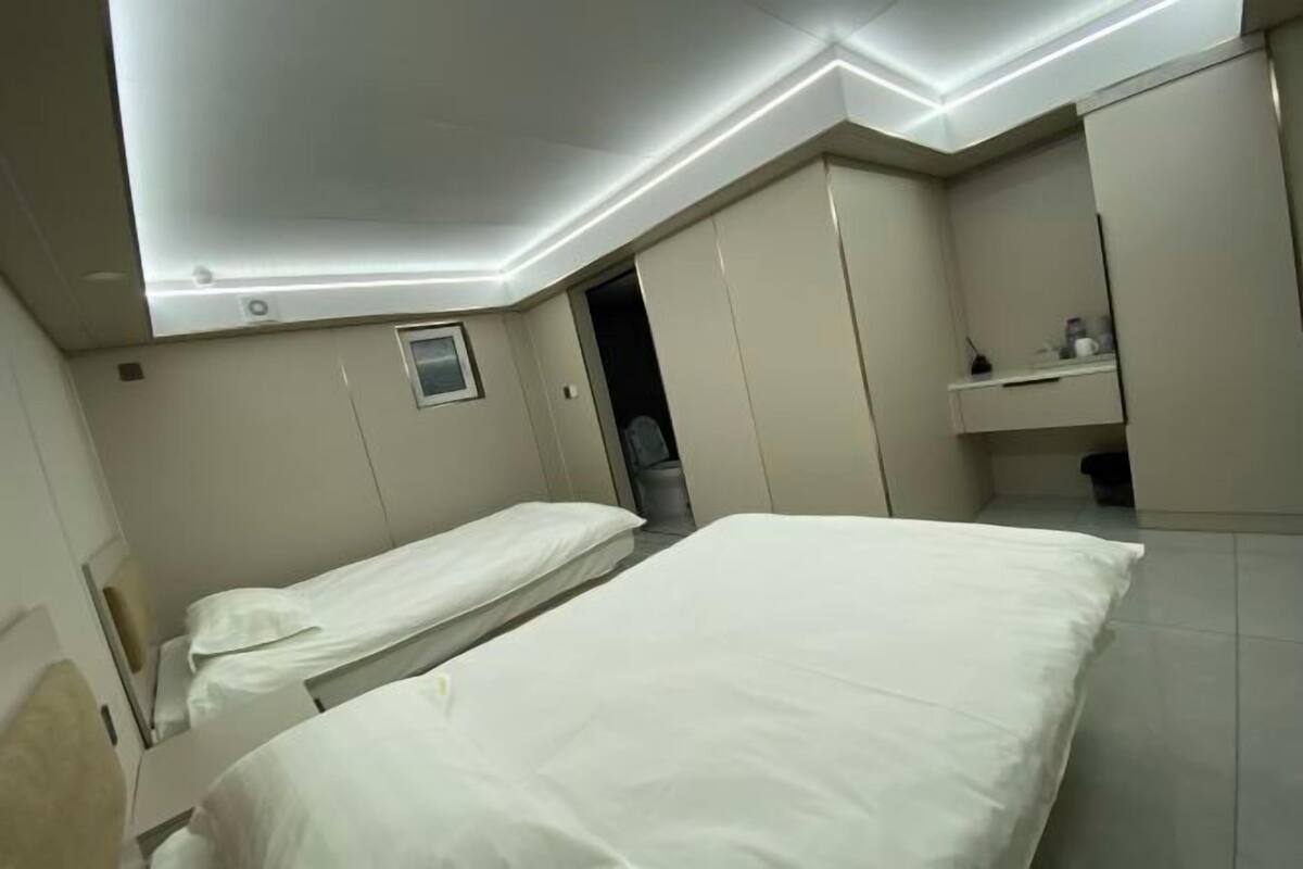 A hotel room with two beds, a small window, a built-in wardrobe, and a bedside table.