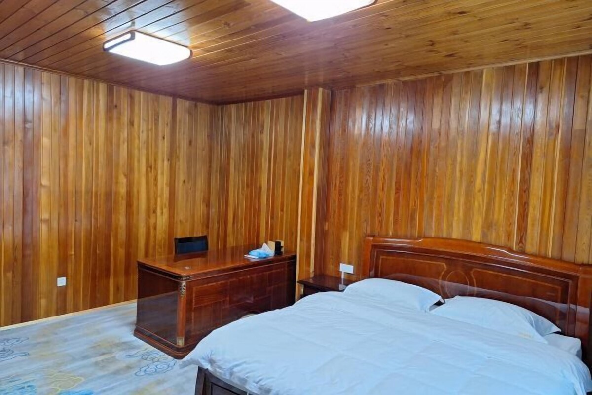 A wooden-paneled room with a bed, bedside table, and a ceiling light fixture.