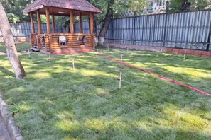 A wooden gazebo with a bench, surrounded by a fenced yard with a red rope marking a path. - Yingbin Garden Hotel (Almaty)