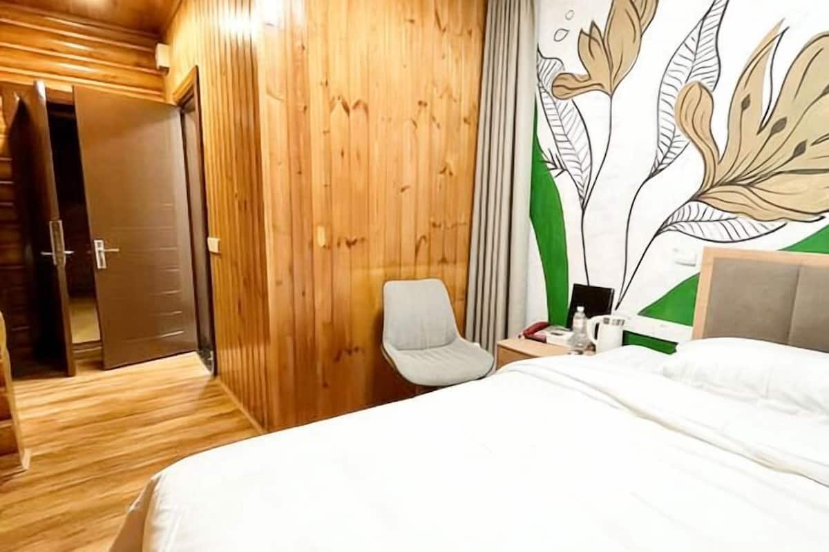 A hotel room with a wooden wall, a bed, a chair, a nightstand, and a wall art piece.