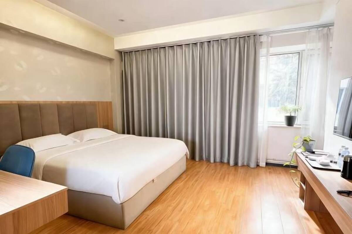 A hotel room with a bed, a desk, a chair, a television, and a window with curtains.