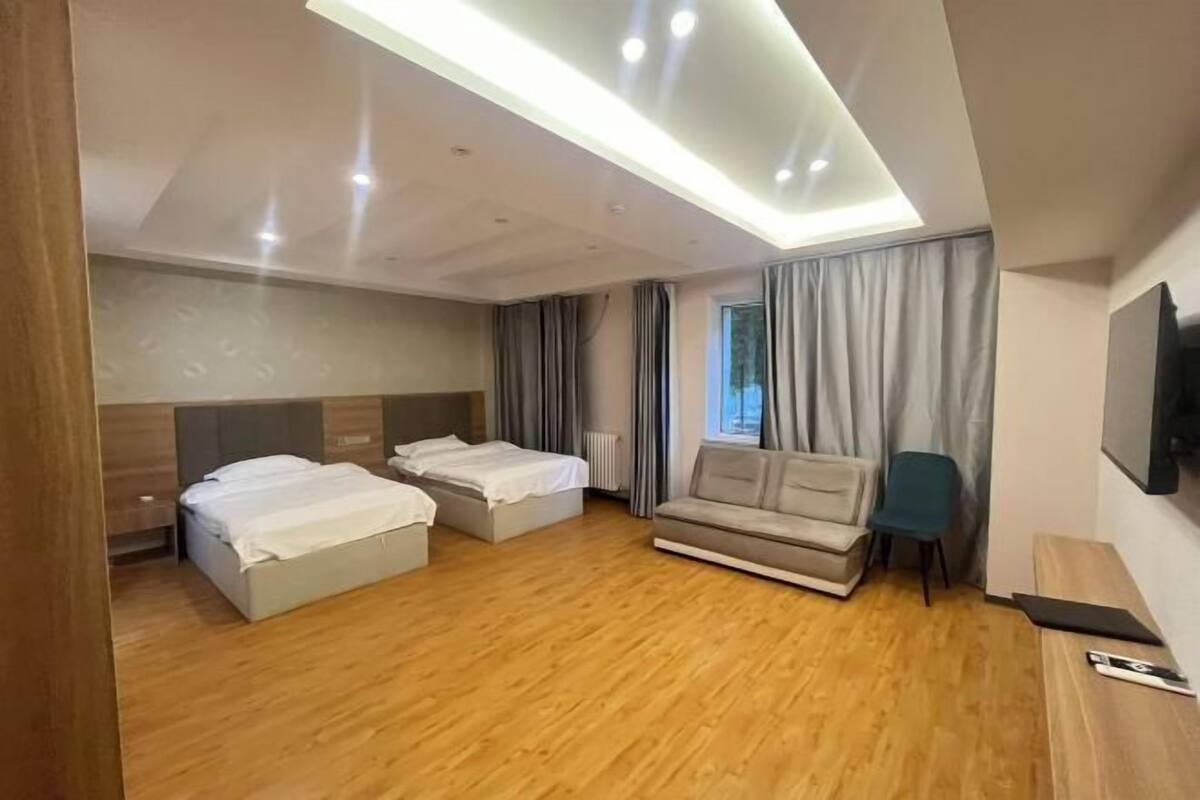 A hotel room with two beds, a sofa, a TV, and a window with curtains.
