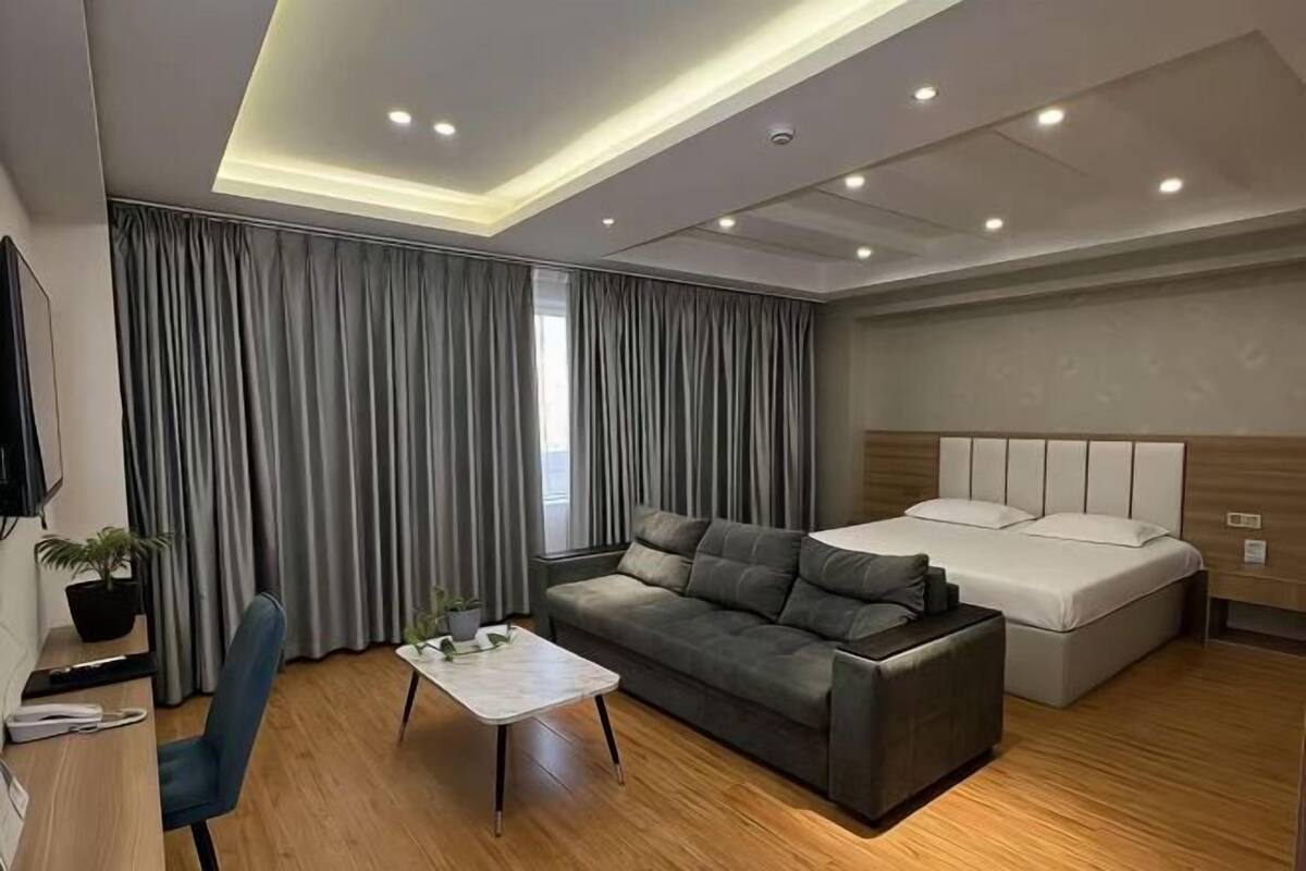 A modern hotel room with a sofa, a bed, a desk, and a TV.