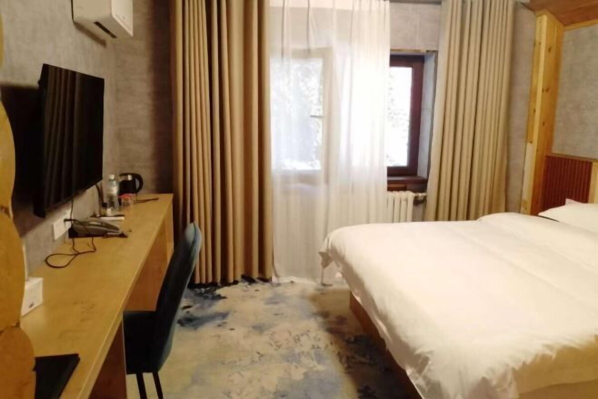 A hotel room with a bed, a desk, a chair, a television, and a window with curtains.