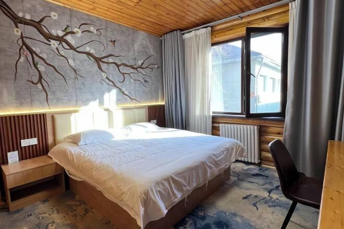 A bedroom with a bed, a nightstand, a chair, a window with curtains, and a wall with a tree mural.